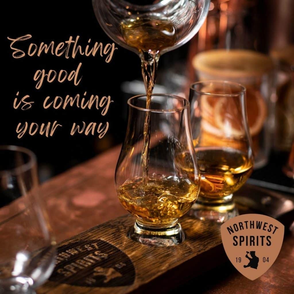 Image of a caramel colored whiskey being poured into a tasting glass sitting on a wooden board resting on a copper bar top. The image is captured mid-pour, evoking a feeling of movement in the glass. There is a text overlay on the image that reads "Something good is coming your way"