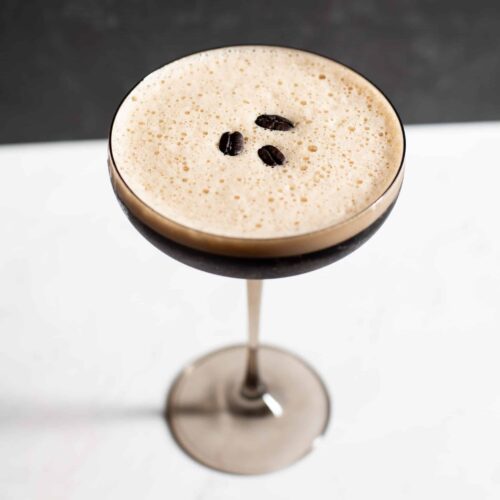 Espresso Euphoria cocktail served in a coupe glass with a creamy espresso foam top, garnished with three coffee beans for health, wealth, and happiness.