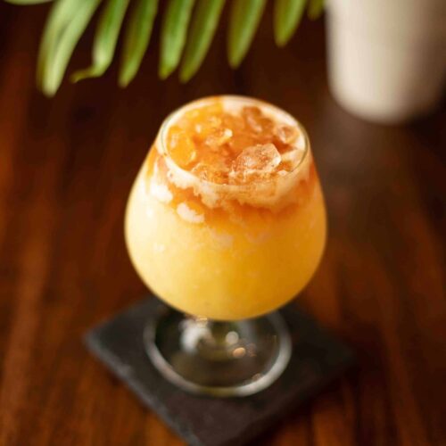 Tropical Painkiller cocktail served in a tulip glass with crushed ice, pineapple wedge garnish, and a dark rum float.