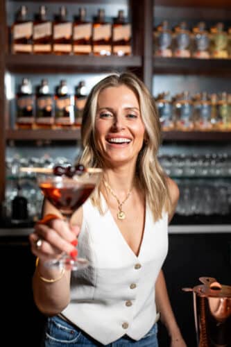 A smiling woman serving a cherry-garnished cocktail in the Tasting Room.